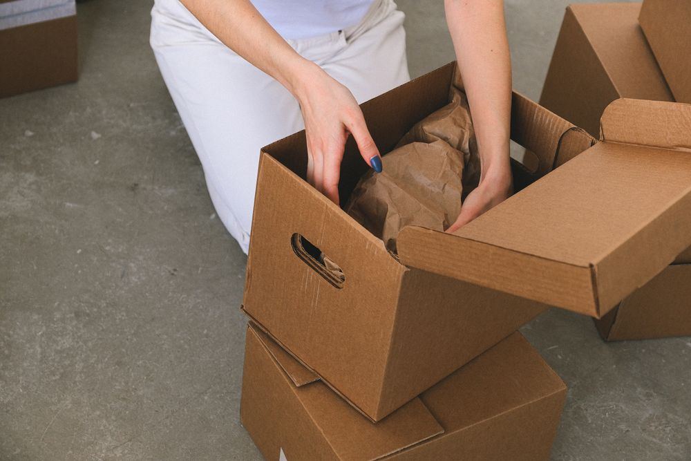 Hands packing a cardboard box during an estate cleanout in an Oklahoma home