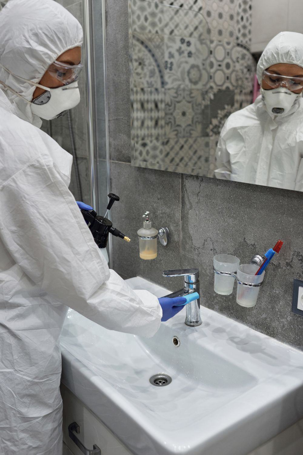 Technician in PPE disinfecting a bathroom sink during biohazard remediation in Oklahoma