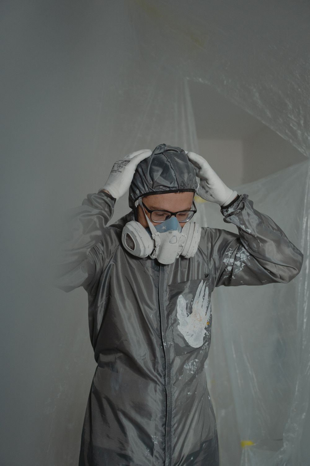Technician adjusting a respirator in front of plastic containment sheeting on a biohazard cleanup job in Oklahoma