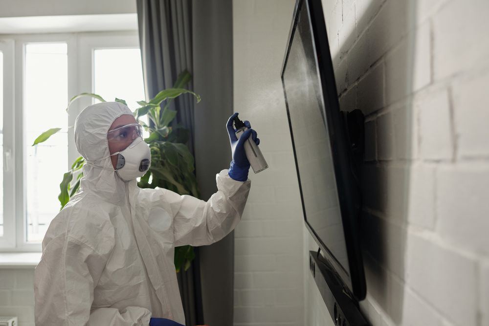 Technician in protective gear disinfecting a wall surface during decomposition stain cleanup in Oklahoma