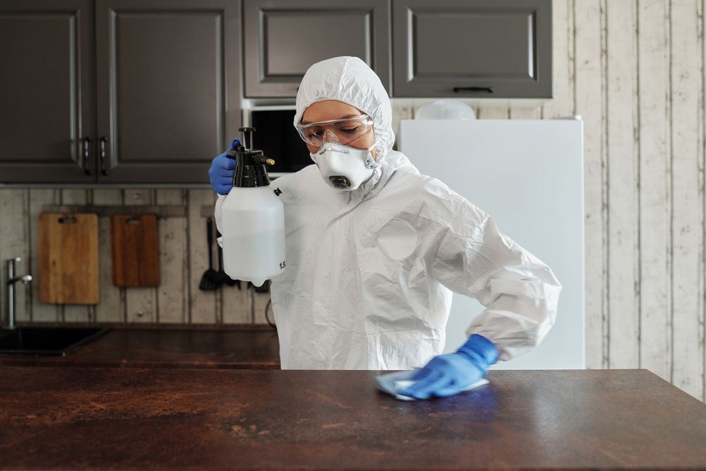 Technician in PPE disinfecting a kitchen counter with a pump sprayer in an Bixby, Oklahoma home