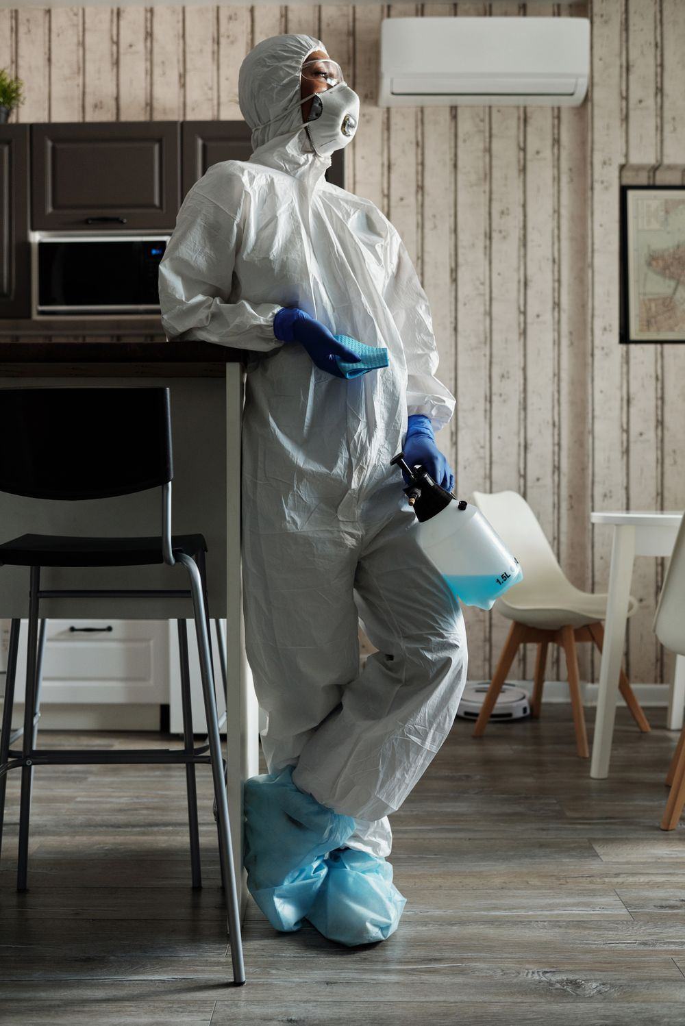 Biohazard technician in full PPE holding disinfection sprayer equipment inside an Oklahoma home