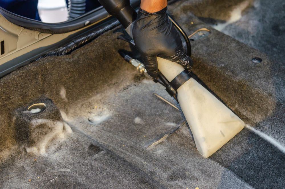 Gloved hand using an extraction tool to clean a vehicle carpet during biohazard cleanup in Oklahoma